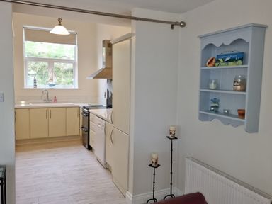A kitchen area with cream cabinets a sink and window and a blue wall shelf with candles and ornaments at Beach House in Duncannon County Wexford