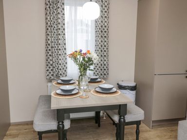 A dining table set with dishes glasses and flowers by a window with patterned curtains at Plot 18 Meadow View in Felton