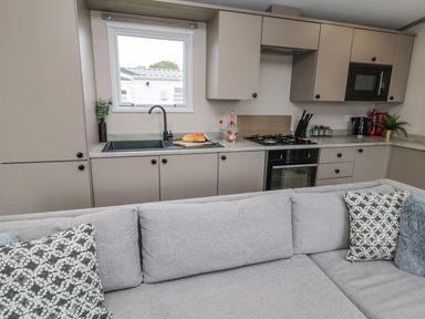 A kitchen with beige cabinets a grey sofa and patterned cushions at Plot 18 Meadow View in Felton