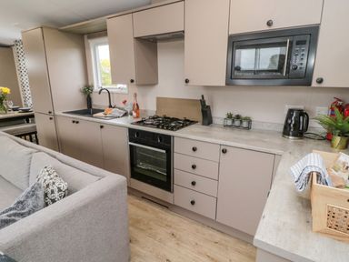 A kitchen with beige cabinets black appliances a gray sofa and wooden flooring at Plot 18 Meadow View in Felton