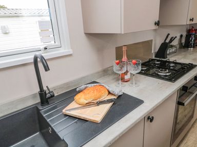 A kitchen countertop with a loaf of bread on a cutting board a knife two glasses with strawberries a bottle of rose wine a stove and a sink at Plot 18 Meadow View in Felton