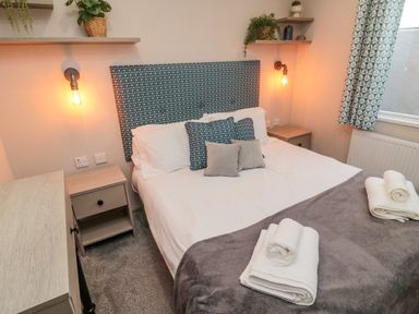 A bedroom with a bed with pillows and towels on a grey blanket bedside tables and shelves with plants at Plot 18 Meadow View in Felton