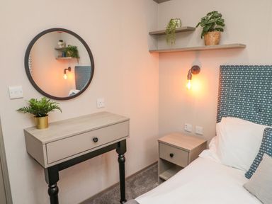 A bedroom with a bed beside a nightstand and a wall-mounted mirror above a small table at Plot 18 Meadow View in Felton