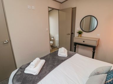 A bedroom with a bed, folded towels, a small table with a plant, a round mirror, and an open door leading to a bathroom at Plot 18 Meadow View in Felton