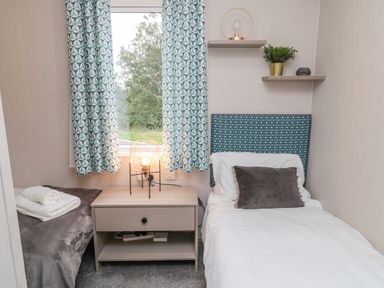 A small bedroom with a single bed a bedside table with a lamp and patterned curtains at Plot 18 Meadow View in Felton