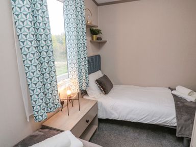 A small bedroom with a single bed a nightstand lamp and patterned curtains at Plot 18 Meadow View in Felton