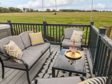 An outdoor seating area with gray cushioned sofa and chairs a black glass coffee table with a gold tray and glasses on a patterned rug at Plot 18 Meadow View Felton