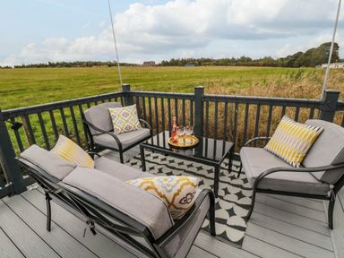An outdoor seating area with gray cushioned chairs and a table with drinks on a deck overlooking a field at Plot 18 Meadow View in Felton