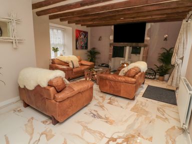 A living room with three brown leather sofas a stone fireplace and wooden ceiling beams at Donni Hall Cottage in Beadnell