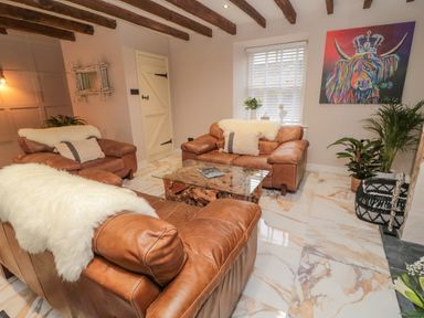 A living room with brown leather sofas a glass coffee table and a colorful animal painting at Donni Hall Cottage in Beadnell
