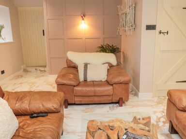 A living room with leather sofas a wooden coffee table a wall light and a cream door at Donni Hall Cottage Beadnell