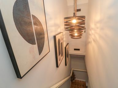 A stairwell with abstract wall art and two hanging light fixtures at Donni Hall Cottage in Beadnell