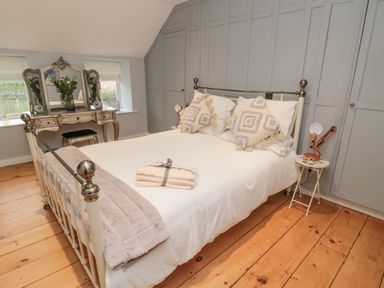 A bedroom with a metal bed, patterned pillows, a vintage vanity with mirror, and wooden floor at Donni Hall Cottage in Beadnell