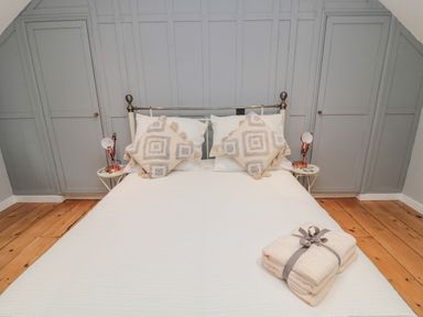 A bedroom with a bed white bedding pillows bedside tables lamps and folded towels on the bed at Donni Hall Cottage in Beadnell