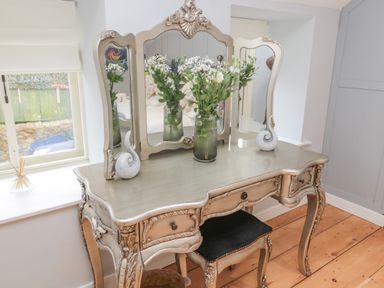 A decorative dressing table with a three-panel mirror and flowers in a vase at Donni Hall Cottage in Beadnell