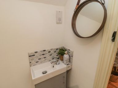 A small sink with a faucet and soap dispenser below a round mirror in a bathroom at Donni Hall Cottage in Beadnell