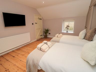 A bedroom with two single beds a wall-mounted tv a wooden floor and a small window at Donni Hall Cottage in Beadnell