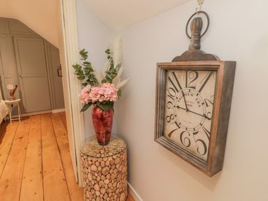 A hallway with a wooden floor a decorative clock on the wall a vase with flowers on a stone base table at Donni Hall Cottage Beadnell