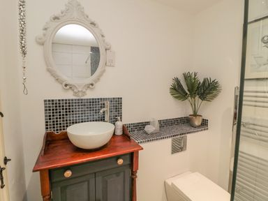 A bathroom with a round mirror above a sink on a wooden cabinet and a tiled shelf with a plant at Donni Hall Cottage in Beadnell