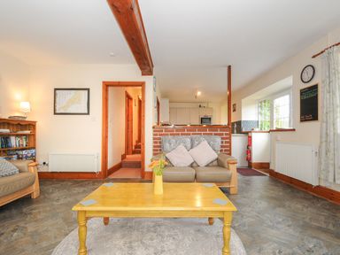 A living room with a yellow coffee table, two sofas, a bookshelf, a wall clock, and a kitchen area at The Wagon House in Lezant near Launceston