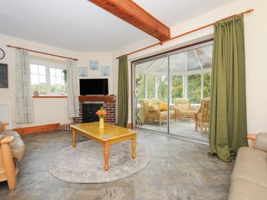 A living room with a wooden coffee table and a TV on a brick fireplace with a view into a conservatory with wicker furniture at The Wagon House in Lezant near Launceston