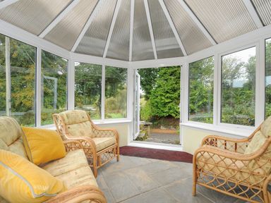 A conservatory with wicker chairs and sofa with cushions and glass windows showing outside at The Wagon House in Lezant near Launceston