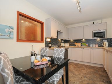 A kitchen with white cabinets a black dining table with cups and pastries at The Wagon House in Lezant near Launceston