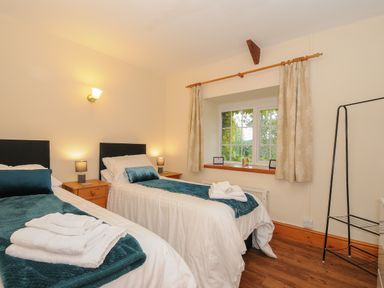 A bedroom with two single beds with teal throws and pillows bedside tables with lamps a window with curtains and a clothes rack at The Wagon House Lezant near Launceston