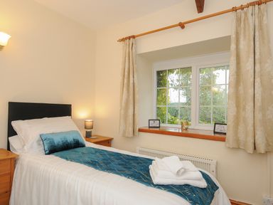 A bedroom with a single bed a blue throw and pillow bedside tables with lamps and a window with curtains at The Wagon House Lezant near Launceston