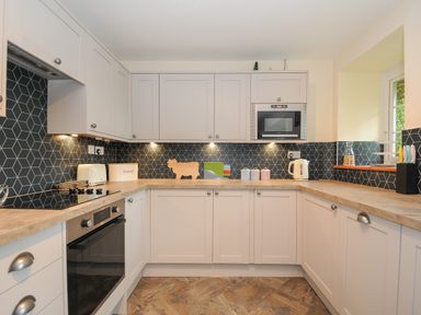 A kitchen with white cabinets a black oven a microwave a toaster a kettle and a window at The Wagon House in Lezant near Launceston
