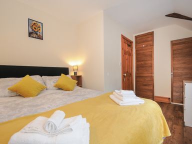 A bedroom with a double bed yellow pillows and blanket wooden doors and a small lamp at The Wagon House in Lezant near Launceston