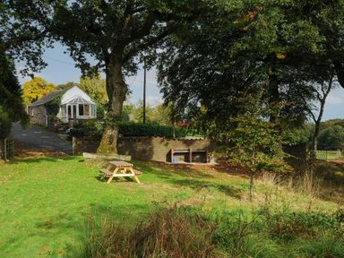 A grassy yard with a wooden picnic table large trees and a stone building in the background at The Wagon House Lezant near Launceston