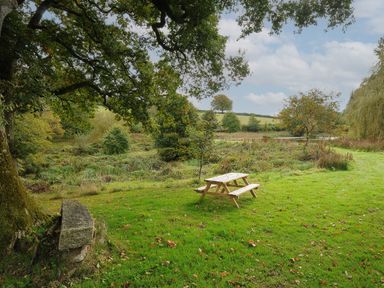 A wooden picnic table on grass with trees and fields in the background at The Wagon House in Lezant near Launceston
