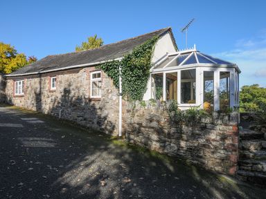 An exterior view of a stone house with white window frames and a white conservatory attached to the side at The Wagon House in Lezant near Launceston