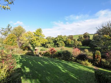 A green lawn with various trees and bushes under a blue sky at The Wagon House in Lezant near Launceston