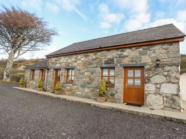 Stone cottage with wooden doors and windows and potted plants outside with a tree nearby at Beech Tree Cottage in Waunfawr