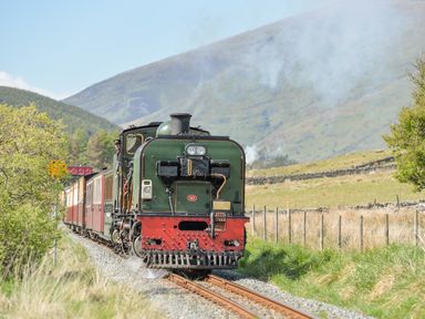 A steam locomotive pulling carriages on tracks in a rural landscape with hills and trees at Beech Tree Cottage in Waunfawr