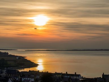A sunset over a body of water with houses and land in the foreground at Beech Tree Cottage in Waunfawr