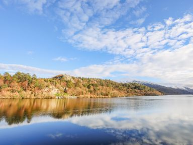 A lake with trees on the shore and snow-capped mountains in the background at Beech Tree Cottage in Waunfawr