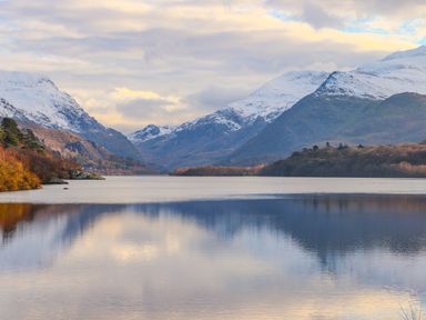 A lake surrounded by mountains with snow on their peaks and trees on the shore at Beech Tree Cottage in Waunfawr