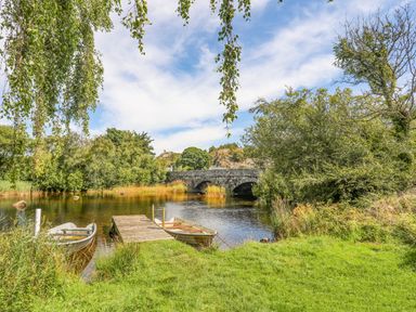 A river with two small boats by a wooden dock and a stone bridge in the background at Beech Tree Cottage in Waunfawr
