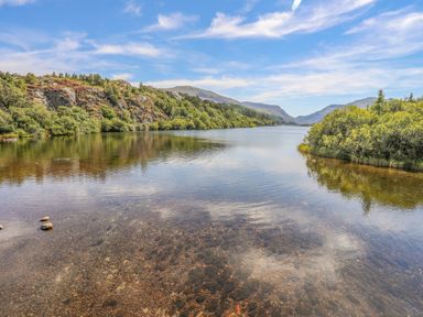 A lake surrounded by trees and hills under a partly cloudy sky at Beech Tree Cottage in Waunfawr