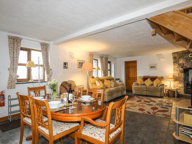 A dining area with a wooden table and chairs and a living room with sofas and a fireplace at Beech Tree Cottage in Waunfawr