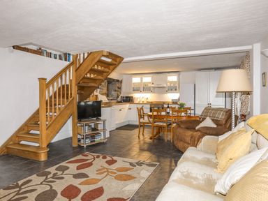 An open plan living room and kitchen with wooden staircase dining table sofas and a television at Beech Tree Cottage in Waunfawr