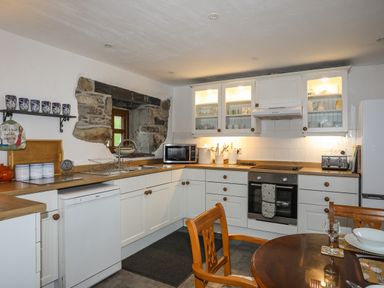 A kitchen with white cabinets wooden countertops a small window with stone surround a dishwasher microwave and oven at Beech Tree Cottage in Waunfawr
