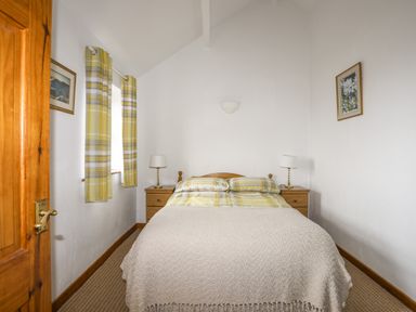 A bedroom with a double bed bedside tables lamps curtains and framed pictures at Beech Tree Cottage in Waunfawr