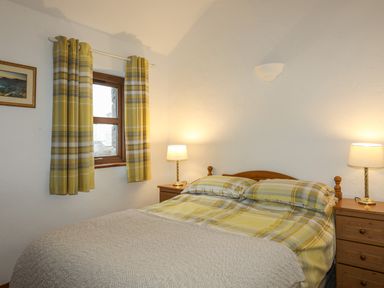 A bedroom with a bed with yellow plaid bedding two bedside tables with lamps and a window with yellow plaid curtains at Beech Tree Cottage in Waunfawr