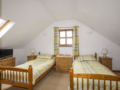 A bedroom with two single beds wooden furniture a small window and yellow plaid curtains at Beech Tree Cottage in Waunfawr
