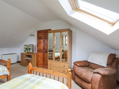 A bedroom with two wooden beds a wooden wardrobe a dressing table and a brown armchair under a skylight at Beech Tree Cottage in Waunfawr