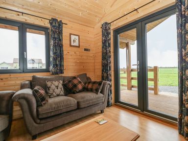 A living room with a brown sofa and pillows next to windows and glass doors leading outside at The Lodge at Crossroads Farm in Middlezoy